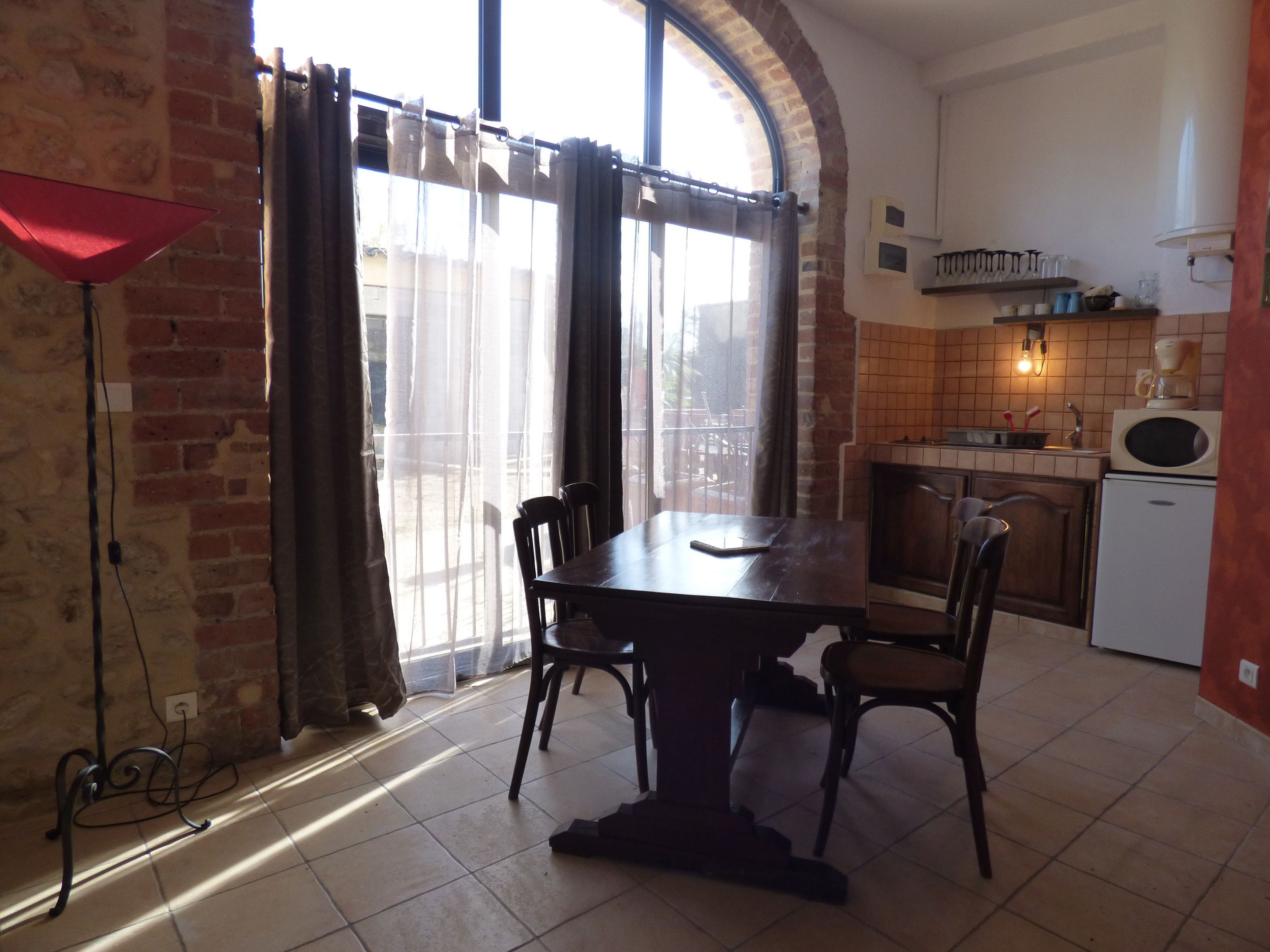 Un comedor con mesa y sillas, una cocina con microondas y pileta, y un ventanal con cortinas.