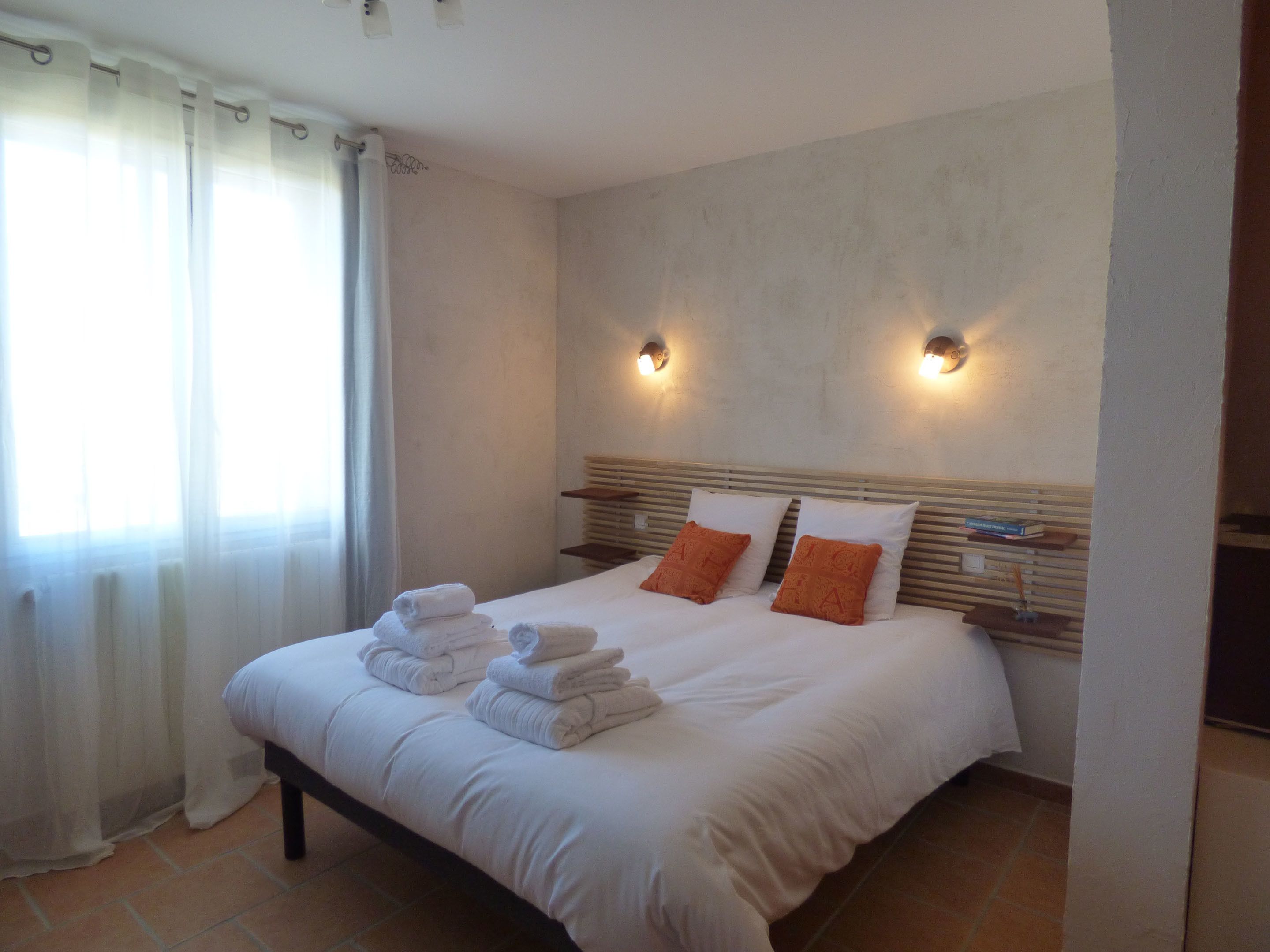 A hotel room with a large bed, two pillows, a nightstand, and a window with curtains.