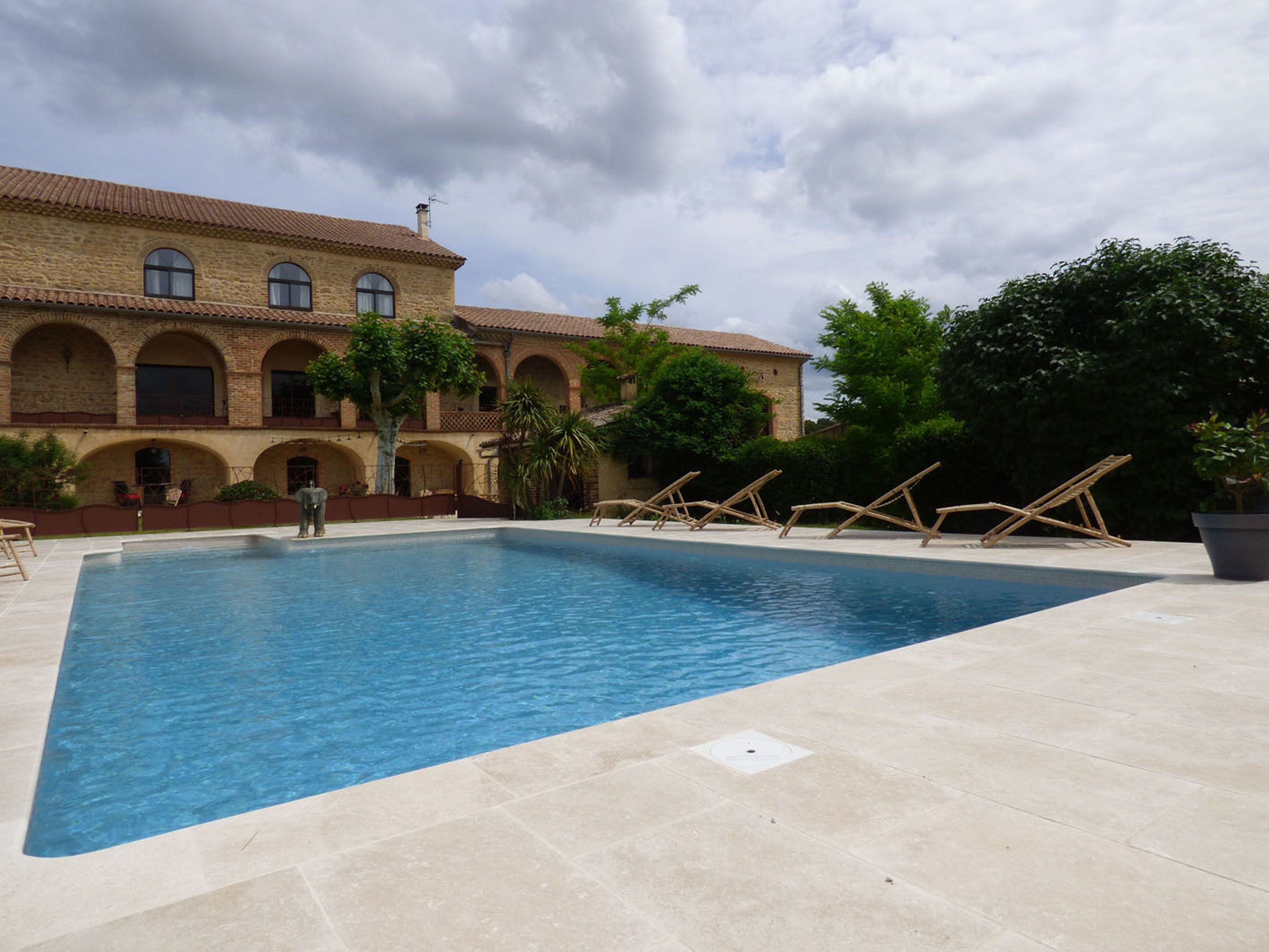 A swimming pool with a tiled deck, surrounded by a building with arched windows and a tiled roof.