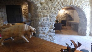 A rustic stone interior with a wooden table, a pig sculpture, and a fish sculpture.