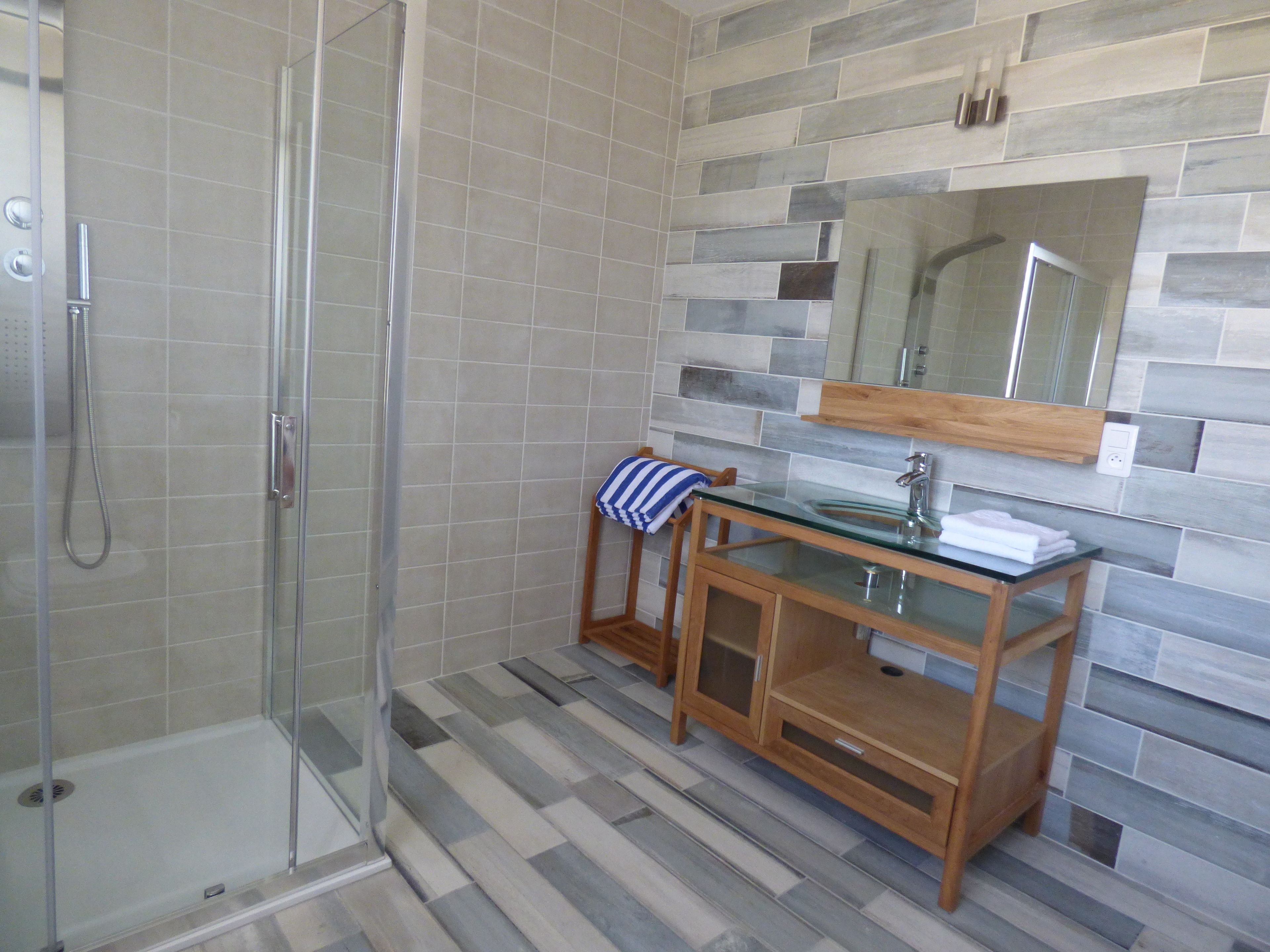 Une douche avec une porte en verre et un meuble-lavabo en bois doté d’un vasque en verre.