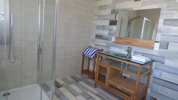 Une douche avec une porte en verre et un meuble-lavabo en bois doté d’un vasque en verre.