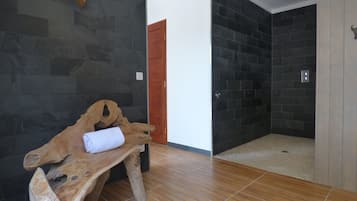 Un baño moderno con paredes de piedra oscura, un banco de madera con una toalla y una zona de ducha.