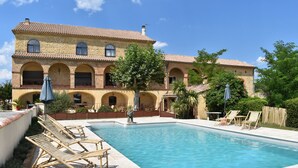 A pool area with lounge chairs and a large building with arched windows and a tiled roof.