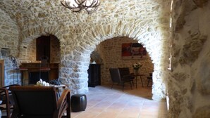 A stone-walled room with a fireplace, a chandelier, and a dining area with chairs and a table.