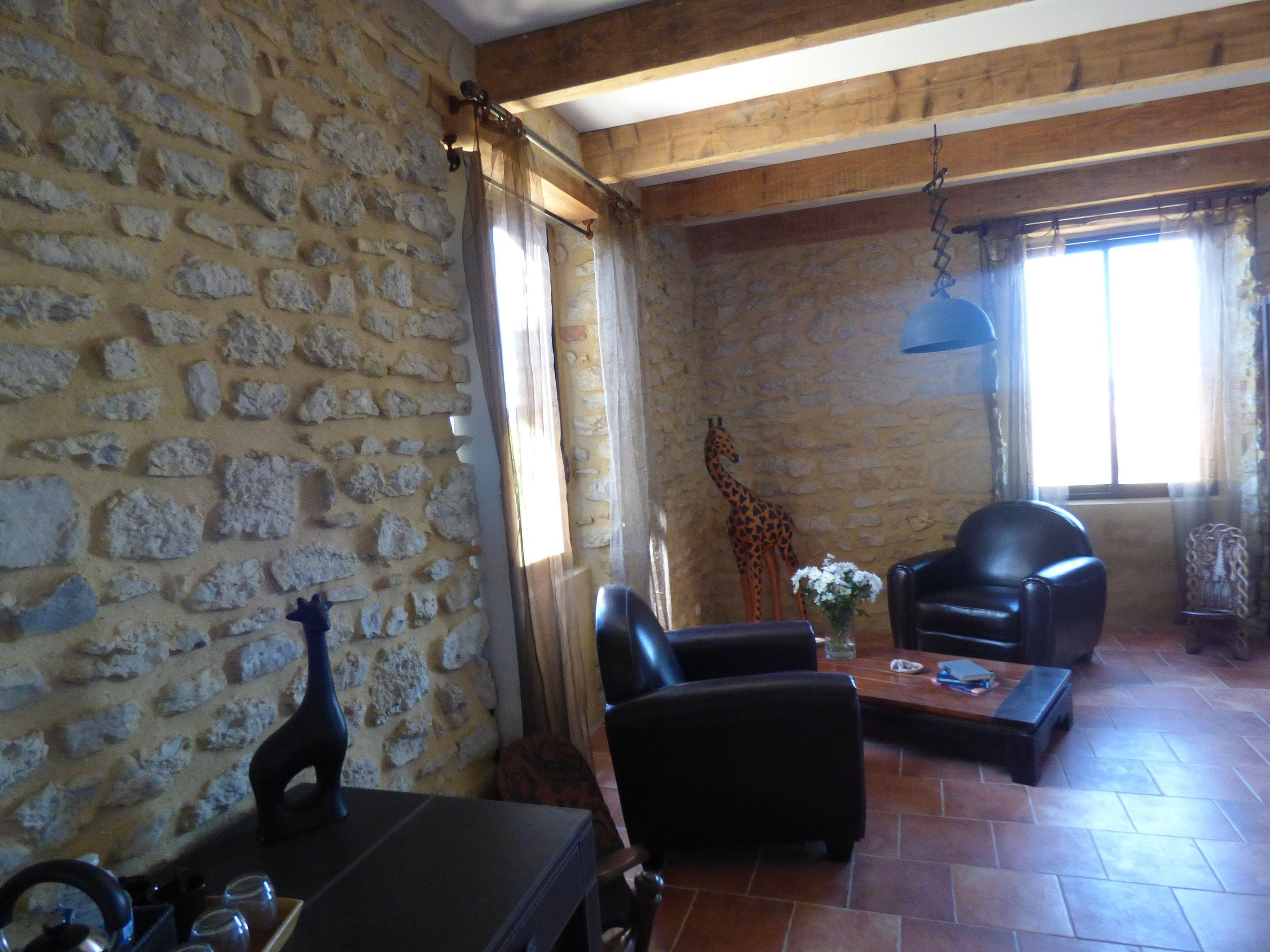A stone-walled room with a wooden ceiling, a giraffe sculpture, a black leather chair, and a coffee table.