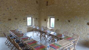 A room with stone walls, wooden tables and chairs, and a hanging light fixture.
