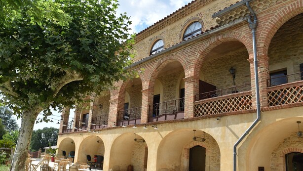 A courtyard with outdoor seating, stone arches, and a building with a tiled roof.