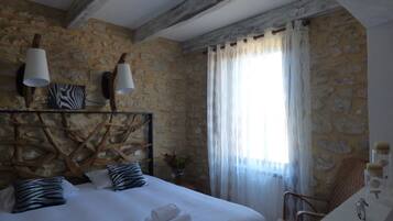 A bedroom with a stone wall, a bed with white linens, two lamps, a zebra-patterned pillow, and a chair.