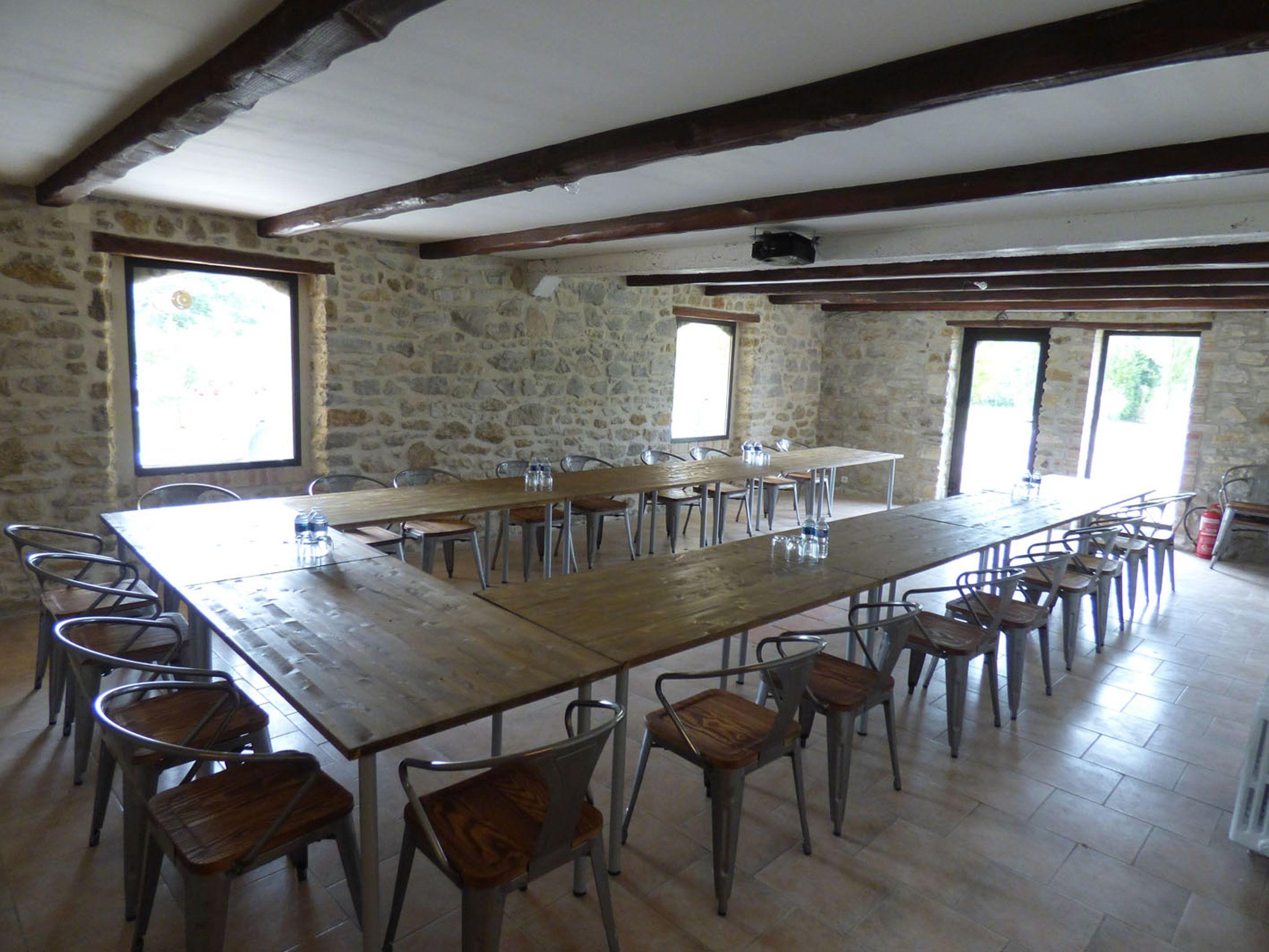 Un comedor rústico con paredes de piedra, mesas de madera y sillas de metal.