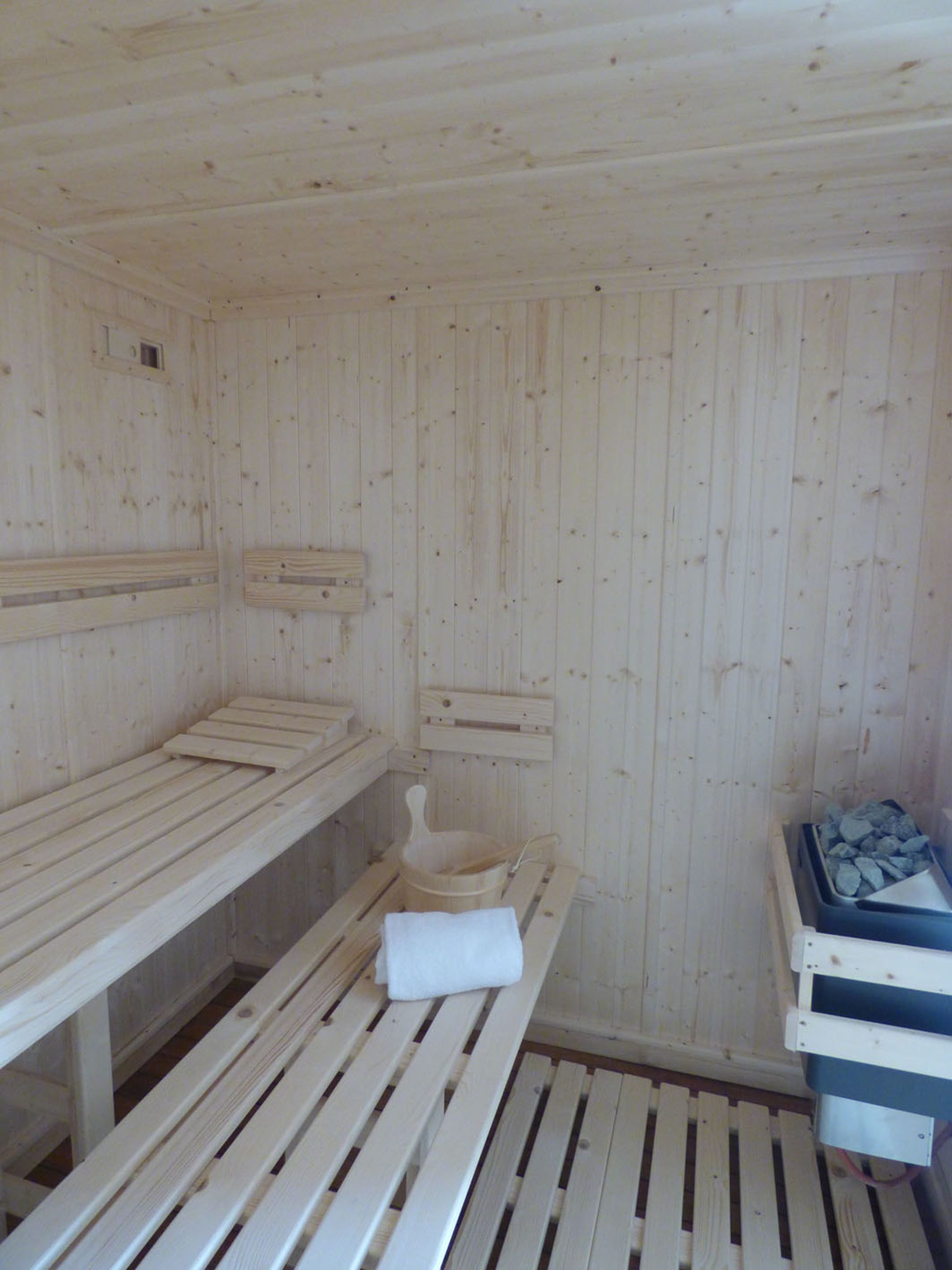 Ein Saunaraum mit Holzbänken und einem Steingefäß.