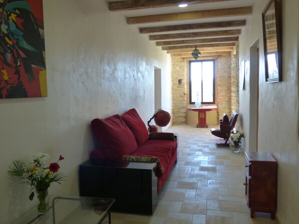 A living room with a red sofa, a glass coffee table, and a vase of flowers. There is a stone wall and a wooden ceiling.