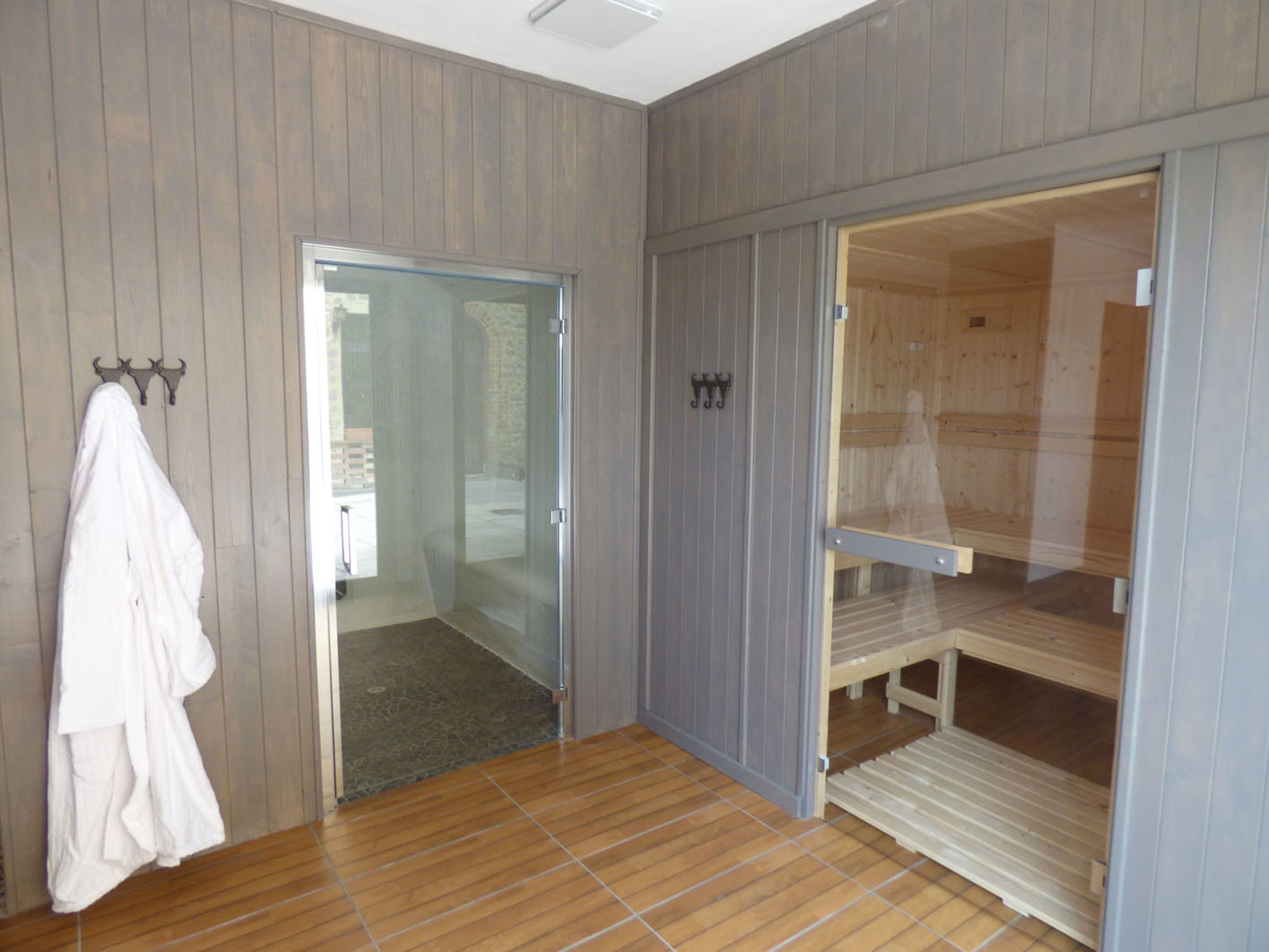 A room with wooden panel walls, a glass door leading outside, a white robe hanging on a hook, and a bed with a wooden frame.