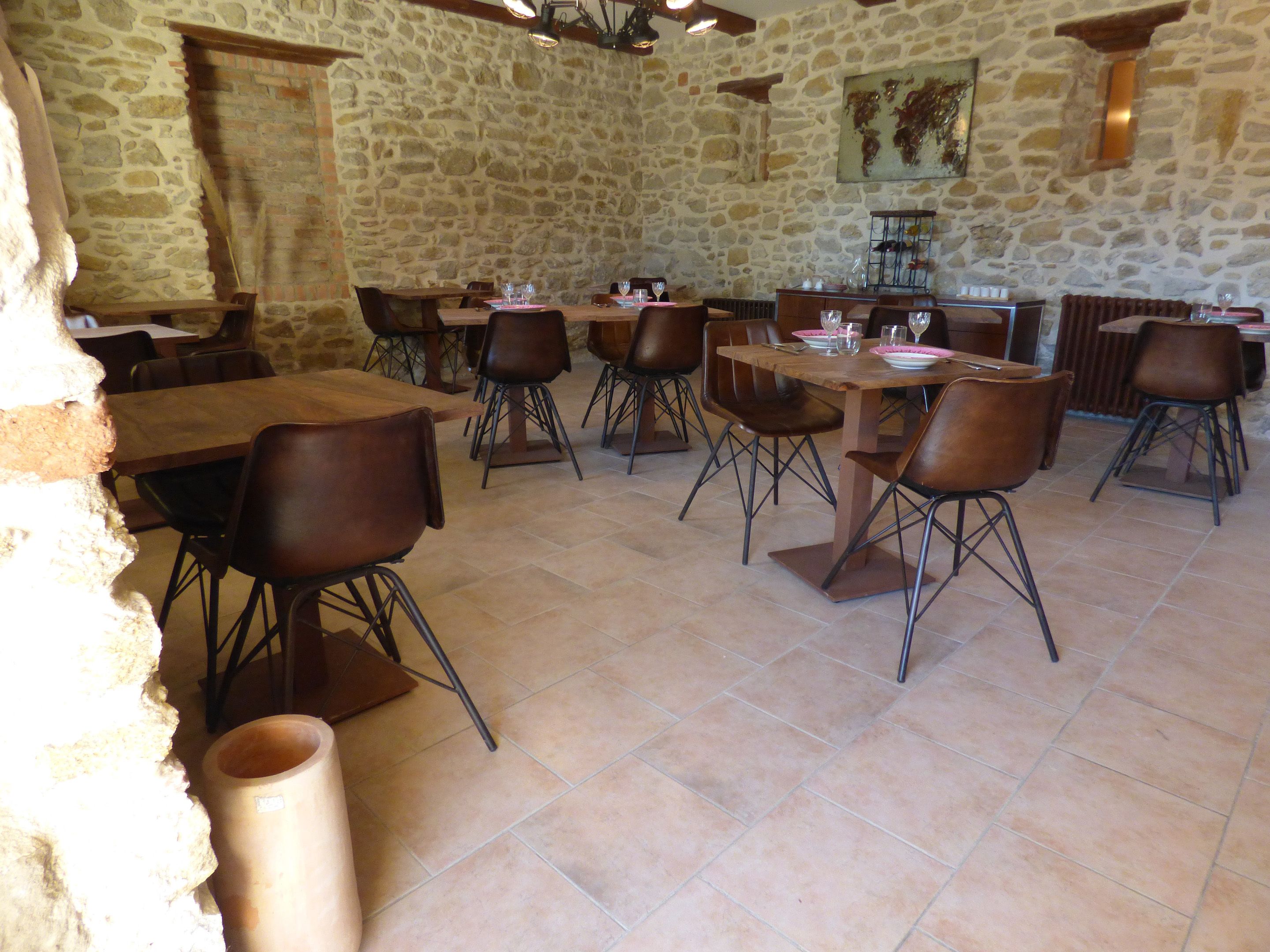 A stone-walled dining area with multiple tables and chairs, a tiled floor, and a rustic ambiance.