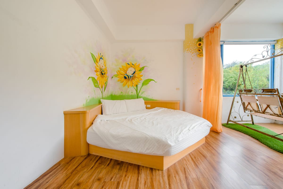 A bedroom with a wooden bed, a wall mural of sunflowers, a swing, and a window with curtains.