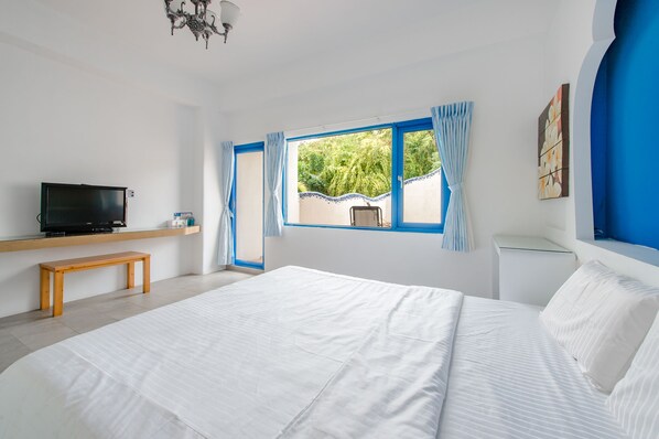A bedroom with a large bed, a wooden bench, a TV, and a window with curtains. - White Lighthouse B&B (Liuqiu)