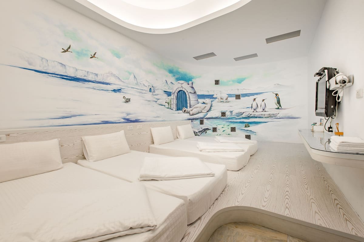 A room with three beds, a large mural of a snowy landscape, and a small pool area.