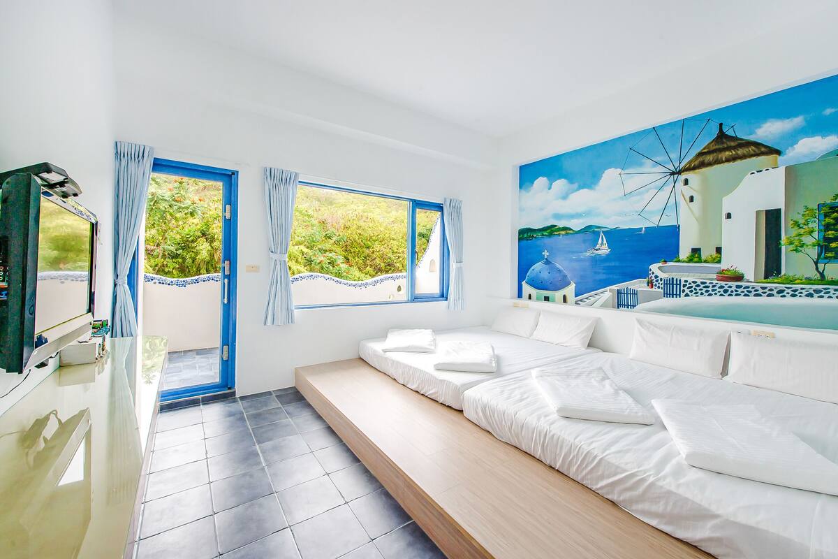 A modern room with a bed, a TV, and a view of a blue sea and windmill.