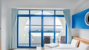 A hotel room with a large sliding glass door leading to a balcony with a view of the sea. There is a bed with white linens and a wooden headboard. - White Lighthouse B&B (Liuqiu)
