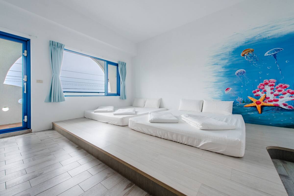 A modern room with a large window, a sofa bed, and a mural of an underwater scene.