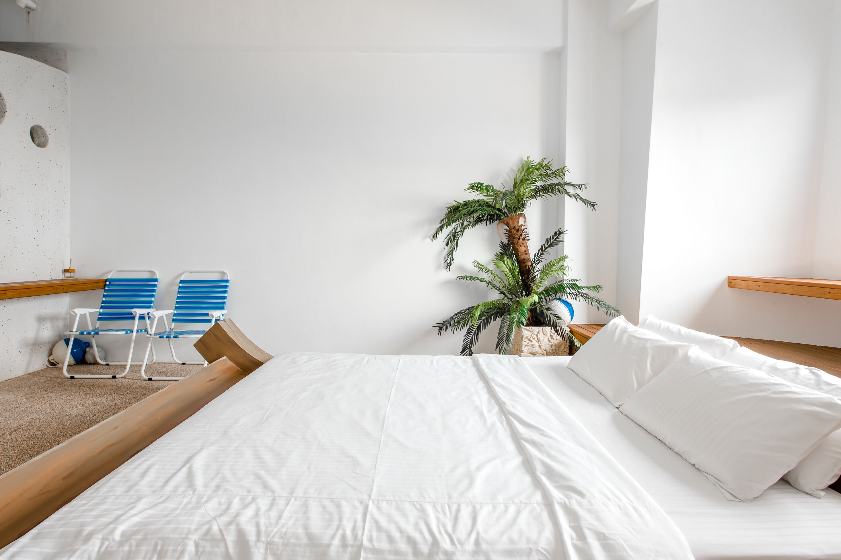 A neatly made bed with white linens, a blue and white striped chair, and a potted plant.