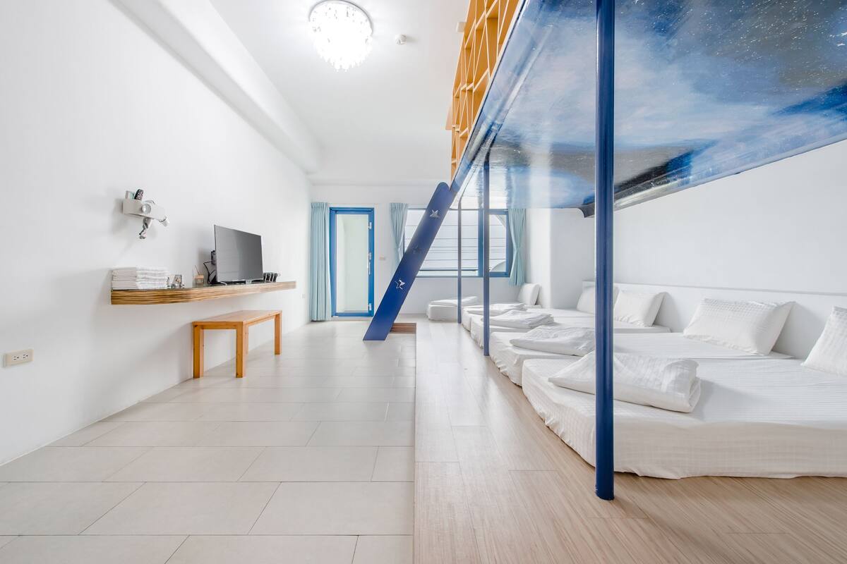 A modern hotel room with a bed, a desk, a TV, and a staircase.
