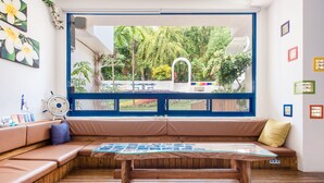 A room with a large window, wooden flooring, a sofa with cushions, a glass-top table, and wall decorations. - White Lighthouse B&B (Liuqiu)