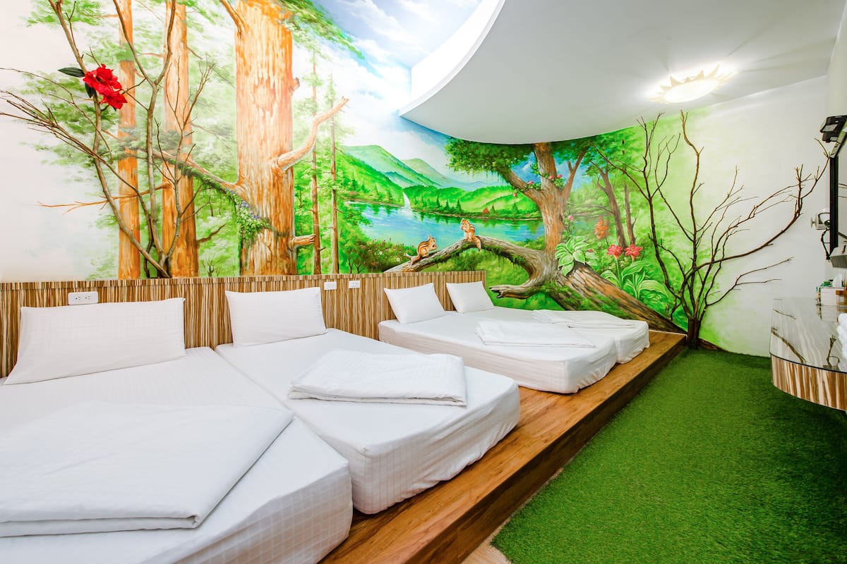 A room with three beds, a mural of a forest scene, and a small table with a mirror.