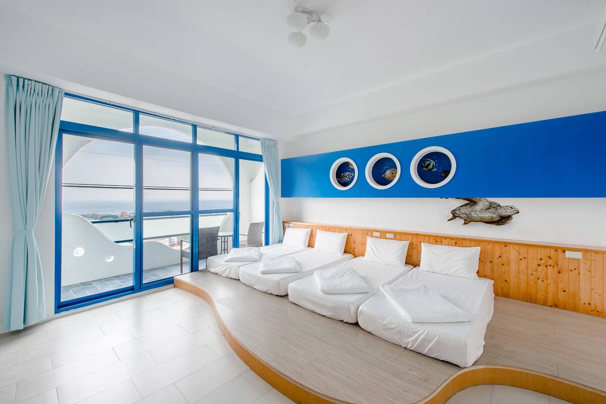 A hotel room with a large window, a wooden headboard, and a bed with white bedding.