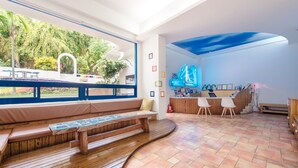 A modern interior with a wooden bench, a reception desk, and a view of greenery outside. - White Lighthouse B&B (Liuqiu)
