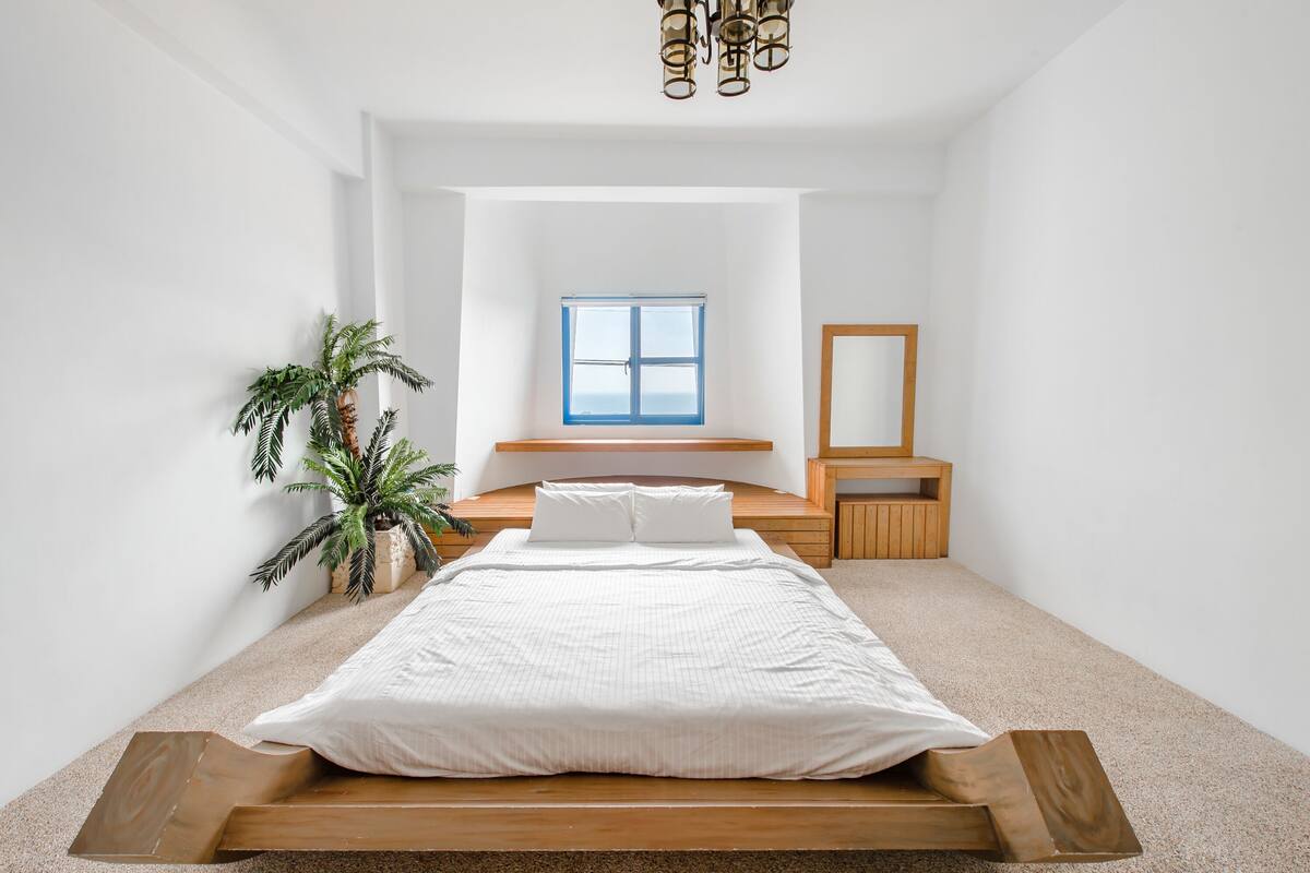 A bedroom with a bed, a window, a plant, and a wooden bench.