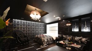 A modern room with a patterned wall, a massage chair, a sofa, a coffee table with a bottle, and a chandelier. - Restay Onoji - Adults Only (Machida)