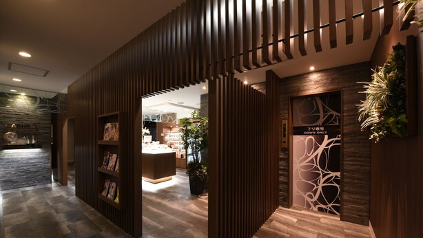 A modern hotel lobby with a wooden reception desk, a glass display case, and a patterned wall design. - Restay Onoji - Adults Only (Machida)