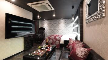 A modern hotel room with a flat-screen TV, a sofa, a coffee table with decorative items, a bed with a patterned bedspread, and a large mirror on the wall.