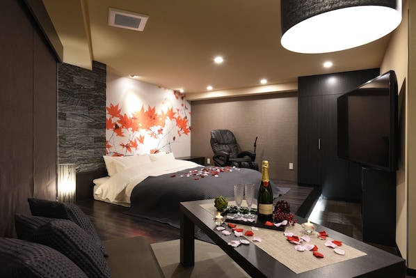 A modern hotel room with a bed, a dining table with a bottle and glasses, a chair, and a television.