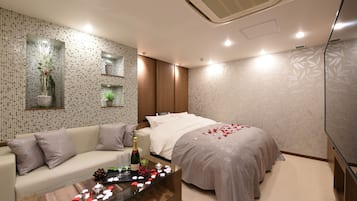 Ein modernes Schlafzimmer mit einem Bett, einem Sofa und einem Glastisch mit einer Flasche und Blumen.