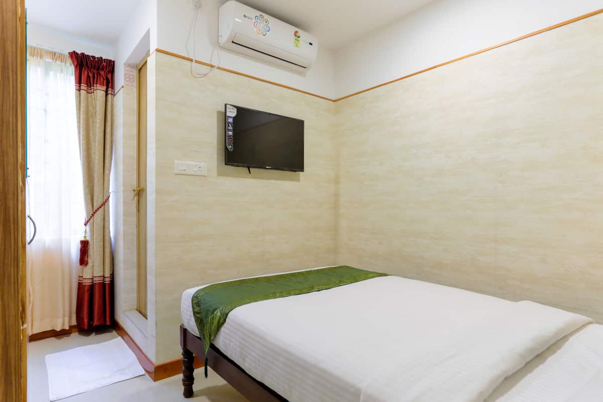 Um quarto com cama, televisão fixada na parede e aparelho de ar condicionado.