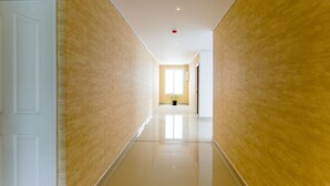 Un pasillo con paredes color crema y un suelo brillante, que conduce a una habitación con ventana y planta.