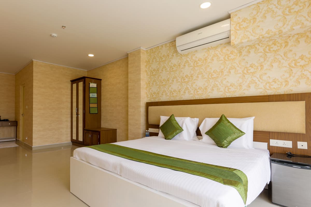 Quarto de hotel com uma cama grande, minibar, guarda-roupa de madeira e ar condicionado na parede.