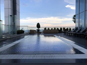 A rooftop infinity pool with lounge chairs and a glass-enclosed shower area. - Vortex Luxury Suite At KLCC (Kuala Lumpur)