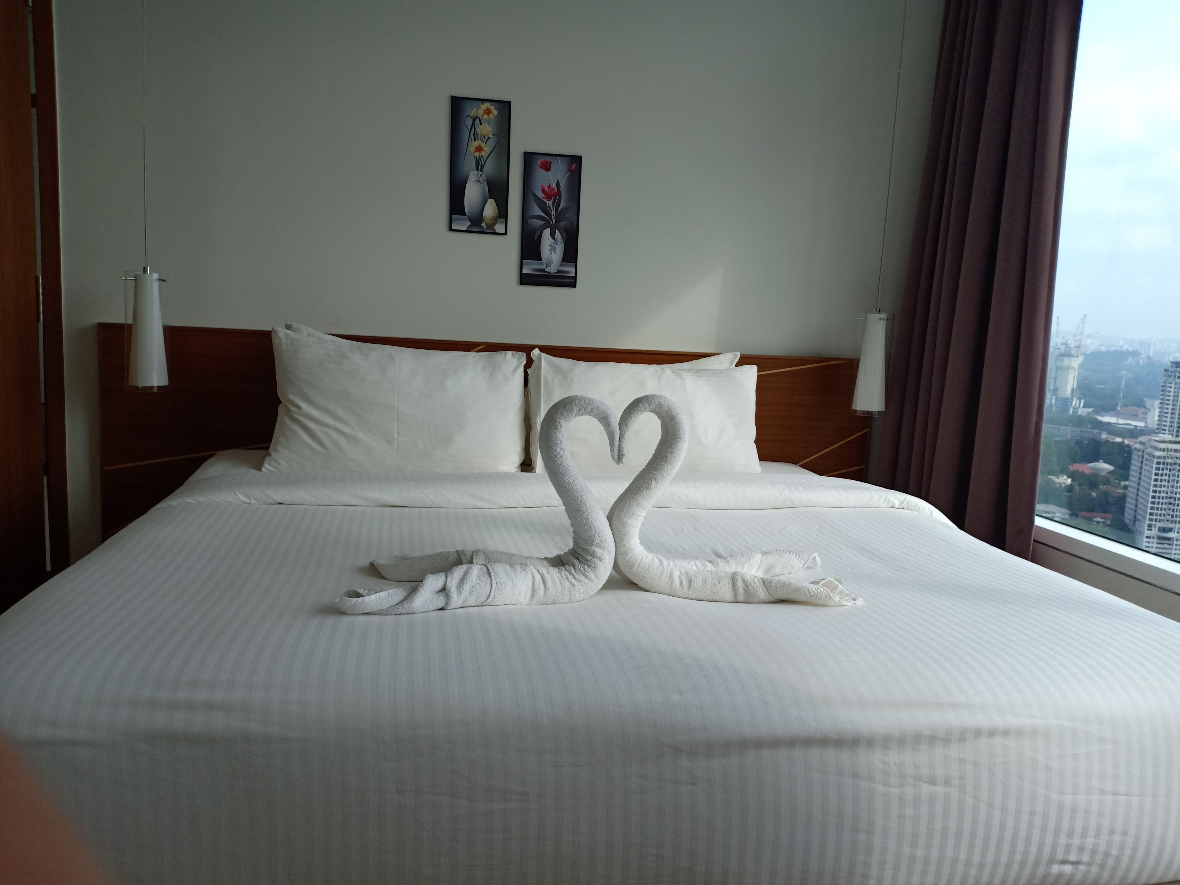 Une chambre d’hôtel avec un lit agrémenté d’une décoration en forme de cygne réalisée avec des serviettes, du linge de lit blanc et deux œuvres d’art encadrées accrochées au mur.