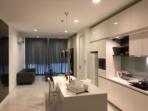 A modern kitchen with white cabinets, a central island, and a dining area with a sofa and curtains. - Vortex Luxury Suite At KLCC (Kuala Lumpur)
