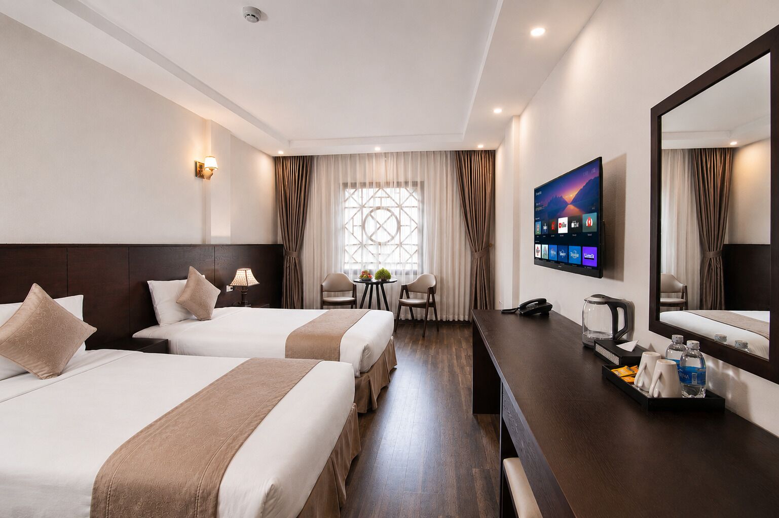 A hotel room with two beds, a desk with a coffee maker, a TV, and a large window with curtains.