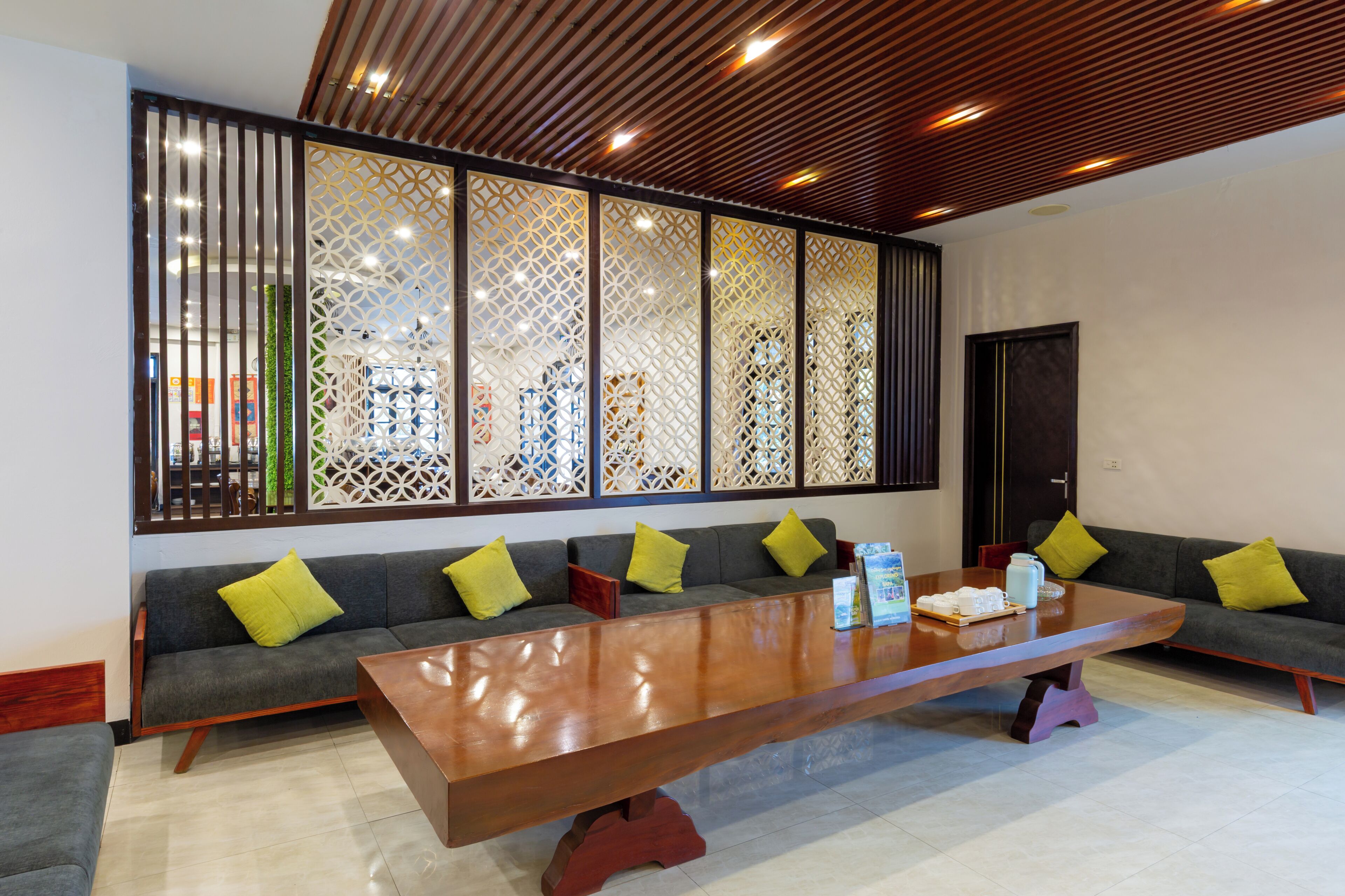 Un salón de conferencias con una larga mesa, sofás grises con cojines amarillos y un separador decorativo con patrones geométricos.