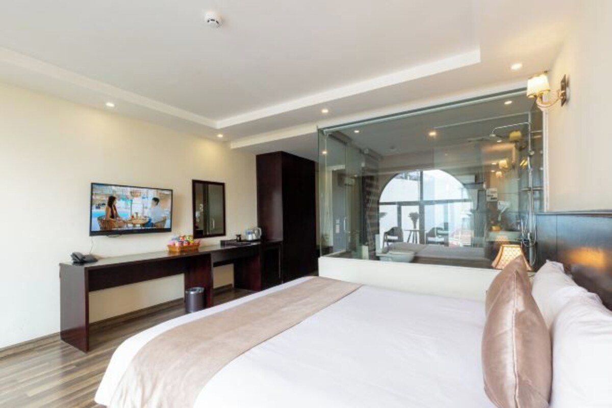 A hotel room with a large bed, a desk, a chair, a television, and a large window.