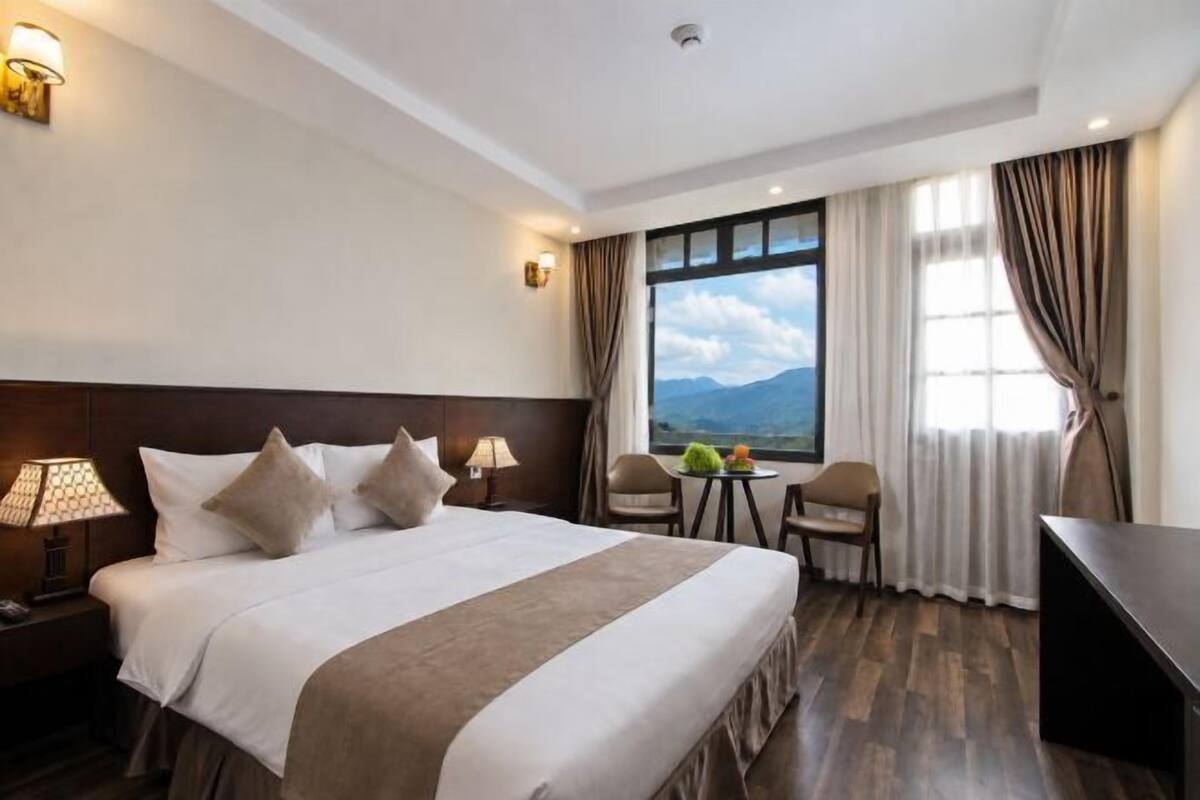 A hotel room with a large bed, a desk, a chair, and a view of the mountains.