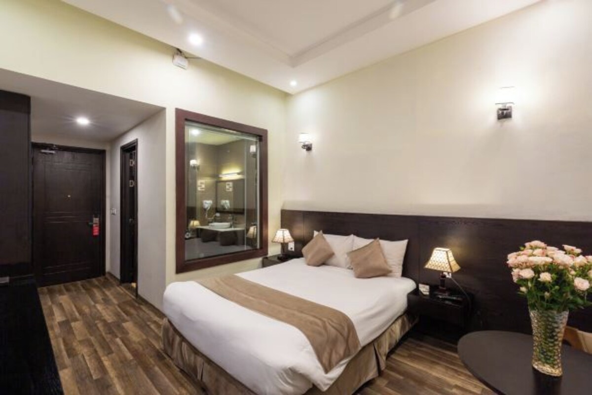 A hotel room with a large bed, bedside tables, a mirror, and a vase of flowers.
