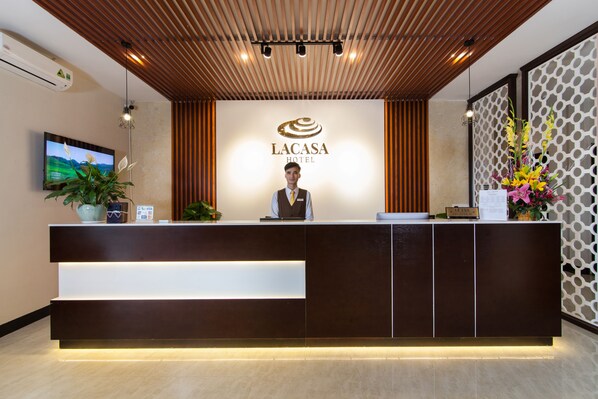 Taulell de recepció a l'Hotel Lacasa amb un disseny modern, una pantalla de televisió i un arranjament floral.