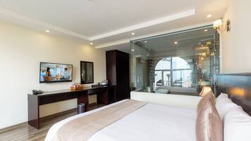 A modern hotel room with a large bed, a desk, a television, and a glass partition.