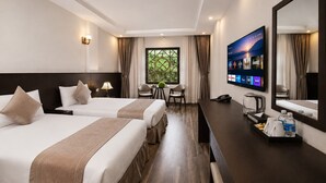 Ett hotellrum med två sängar, ett skrivbord med en tv, en kaffebryggare och ett fönster med gardiner.